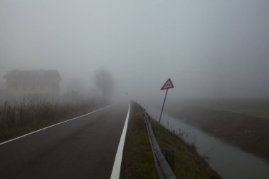 Sonbaharda sisli bir günde bir su akıntısı ile çevrili köy yolu