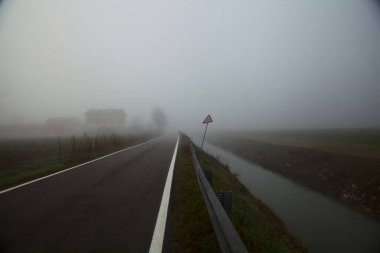 Sonbaharda sisli bir günde bir su akıntısı ile çevrili köy yolu