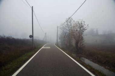 Kışın sisli bir günde çıplak ağaçlar ve tahta sütunlarla dar bir köy yolu.