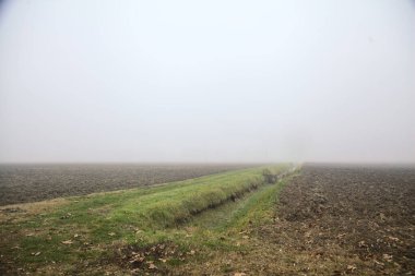 Kışın sisli bir günde sürülen tarlalar arasındaki sulama kanalı