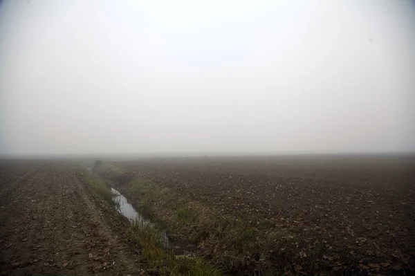 Ploughed field with a irrigation channel on a foggy day in winter