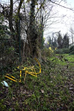 Bulutlu bir günde, parktaki terk edilmiş bir binanın çitlerinin yanında sarı bir bisikletin kalıntıları.