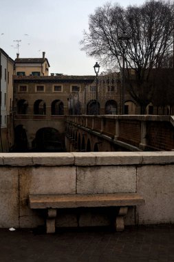 Bench on a wall in front of a stream of water in a town on a cloudy day at sunset