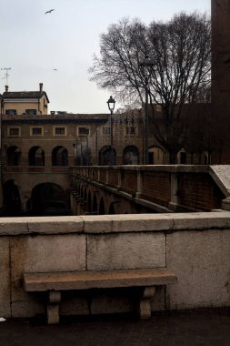 Bench on a wall in front of a stream of water in a town on a cloudy day at sunset
