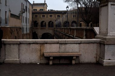 Bench on a wall in front of a stream of water in a town on a cloudy day at sunset