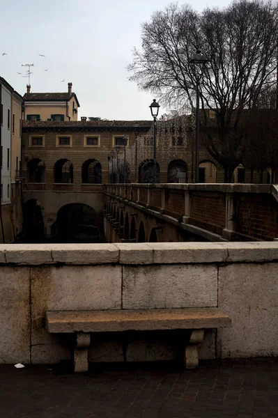 Bench on a wall in front of a stream of water in a town on a cloudy day at sunset