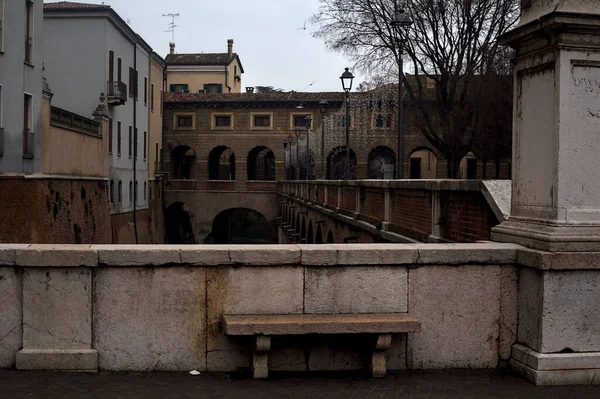 Bench on a wall in front of a stream of water in a town on a cloudy day at sunset