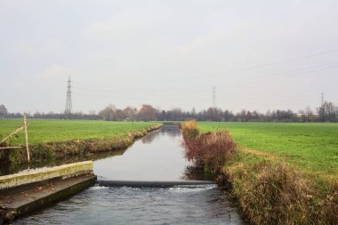 Stream of water between cultivated fields on an overcast day in the italian countryside