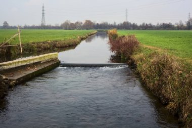 Stream of water between cultivated fields on an overcast day in the italian countryside