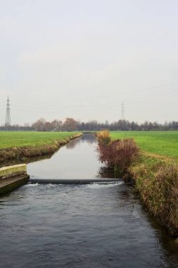Stream of water between cultivated fields on an overcast day in the italian countryside