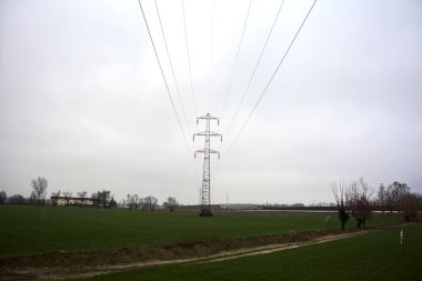 Electricity pylon in a cultivated field next to a highway on a cloudy day in the italian countryside