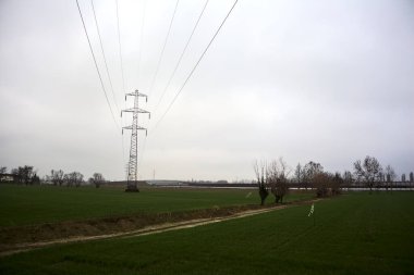 Electricity pylon in a cultivated field next to a highway on a cloudy day in the italian countryside