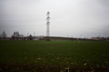 Electricity pylon in a cultivated field next to a highway on a cloudy day in the italian countryside