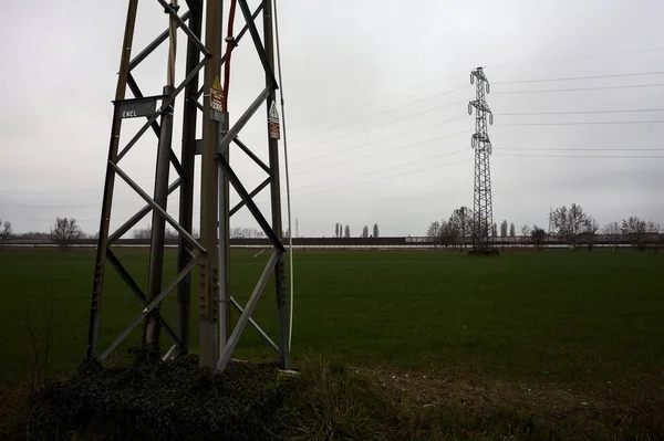 Electricity pylon in a cultivated field next to a highway on a cloudy day in the italian countryside