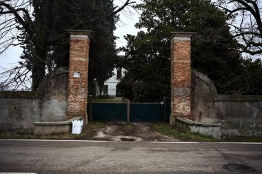 Gate and boundary wall of a country house by the edge of a road on a cloudy day