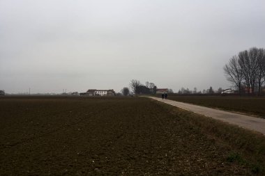Narrow road between ploughed fields on a cloudy day in the italian countryside