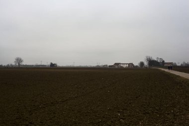 Narrow road between ploughed fields on a cloudy day in the italian countryside
