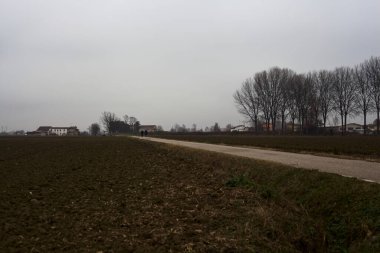 Narrow road between ploughed fields on a cloudy day in the italian countryside