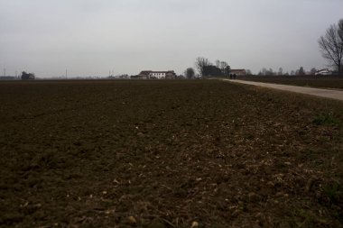 Narrow road between ploughed fields on a cloudy day in the italian countryside