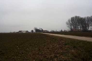Narrow road between ploughed fields on a cloudy day in the italian countryside