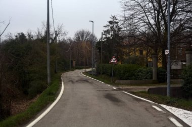 Country road bordered by wooden pylons and fields with a group of houses on a cloudy day