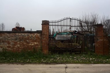 Gate in a brick boundary wall at the edge of a road with building equipments behind the grating in the italian countryside