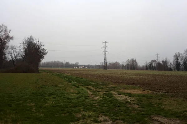 Electricity pylon in a cultivated field next to a highway on a cloudy day in the italian countryside