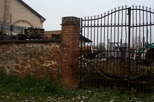 Gate in a brick boundary wall at the edge of a road with building equipments behind the grating in the italian countryside