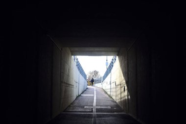 Man walking in an alleyway under a road on a cloudy day