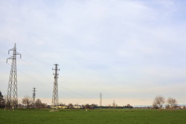 Cultivated field with electricity pylons and over head cables on a cloudy day in the italian countryside