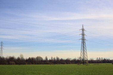 Cultivated field with electricity pylons and over head cables on a cloudy day in the italian countryside