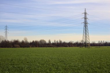 Cultivated field with electricity pylons and over head cables on a cloudy day in the italian countryside