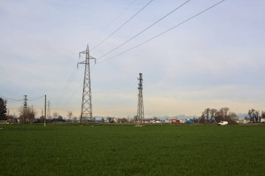 Cultivated field with electricity pylons and over head cables on a cloudy day in the italian countryside