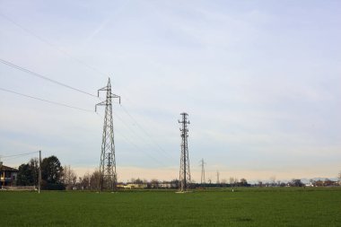 Country road between fields with bare trees and electricity pylons with over head cables on a cloudy day