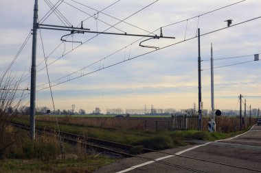 Railroad crossing next to a field on a cloudy day in the italian countryside