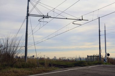 Railroad crossing next to a field on a cloudy day in the italian countryside