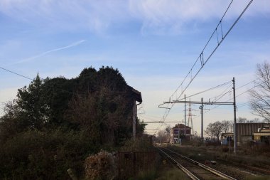 Abandoned building covered by ivy by the edge of a railroad track on a cloudy day in the italian countryside