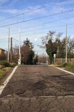 Railroad crossing next to a field on a cloudy day in the italian countryside