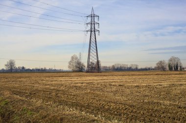 Rows of electricity pylons and power lines over cultivated fields on a winter day in the italian countryside