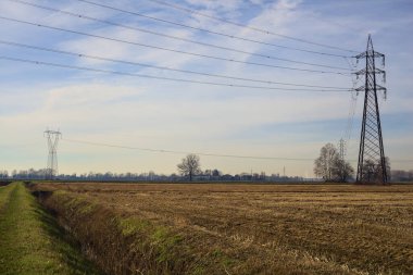 Rows of electricity pylons and power lines over cultivated fields on a winter day in the italian countryside