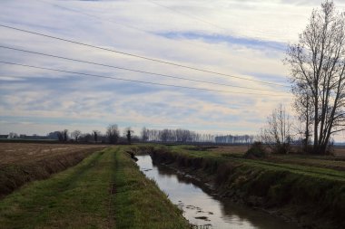 Path between cultivated fields and bordered by streams of water in the italian countryside