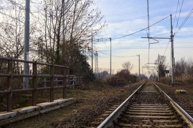 Railroad track borderd by bare trees that stretches to the horizon in the italian countryside in winter