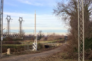 Small country road with a bridge over a stream of water next to a substation in the italian countryside
