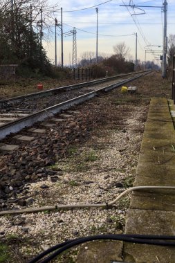 Railroad track borderd by bare trees that stretches to the horizon in the italian countryside in winter