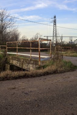 Small country road with a bridge over a stream of water next to a substation in the italian countryside