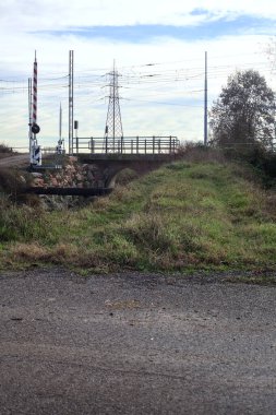 Trail bordered by a stream of water with a railroad crossing over an embankment in the italian countryside