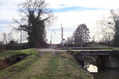 Trail bordered by a stream of water with a railroad crossing over an embankment in the italian countryside