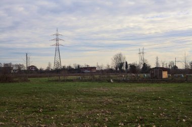 Open space with trees and a pylon in the distance on a cloudy day in the italian countryside