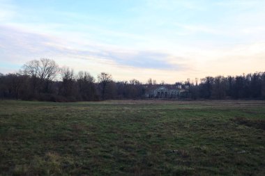 Çıplak ağaçlarla dolu patikanın yanındaki çayır ve gün batımında parkta bir köşk.