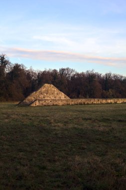 Günbatımında İtalya kırsalında bir ormanın yanındaki çayırda bir manastırın kalıntıları.